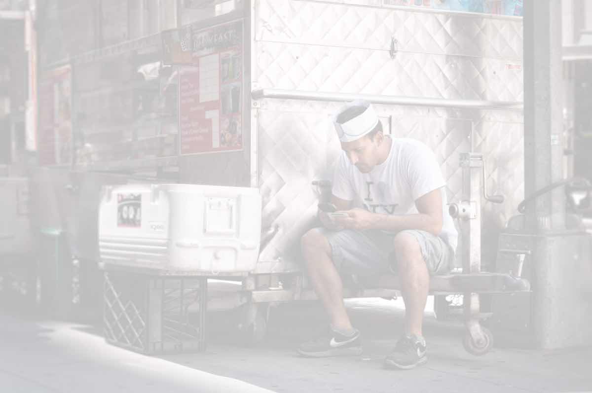 A man checking his phone outside the food cart where he works
